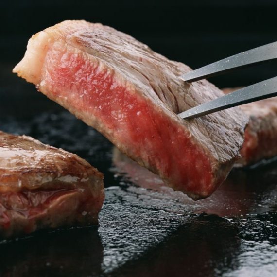 熱い鉄板の上でジューシーに焼き上げられる厚切り和牛ステーキ。香ばしく焼き色のついた表面と、美しいミディアムレアのピンク色の断面